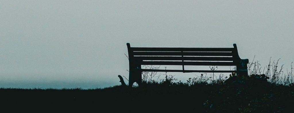 Image shows a silhouette of an empty park bench
