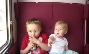 A young brother and sister sit next to each other on a train