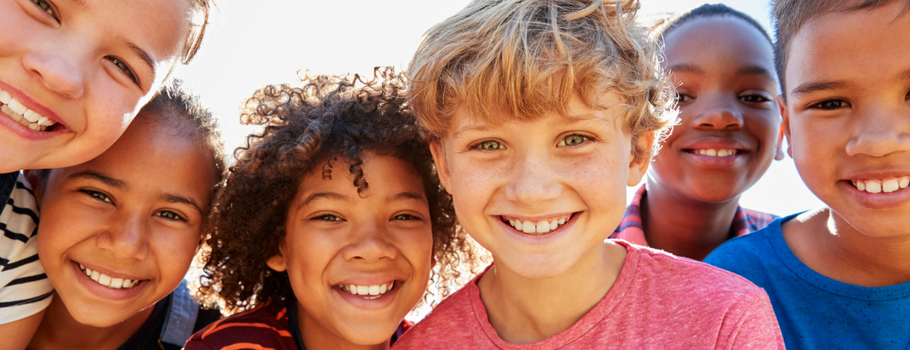 Close up shot of a row of children's faces, bustling close together, grinning