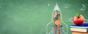A stack of colourful school books with a shiny read apple on top and a pot of coloured pencils sit against a greenish chalkboard, that has a rocket drawn around the pencil pot