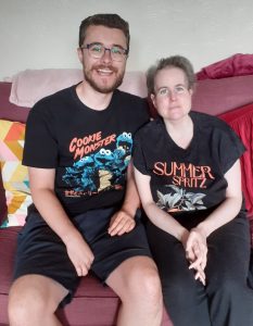 Steven and his sister Rhianna sit close together, smiling at the camera. Both are wearing black t-shirts, Steven's says 'Cookie Monster', Rhianna's says 'Summer Spritz'.