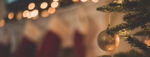 Blurred festive background image showing christmas tree branches, a gold bauble, festive lights and stockings