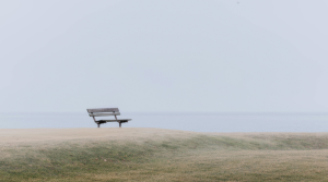 Empty bench on a hillside, looking over a grey sky and pale sea