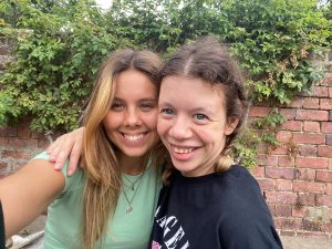 Jamie and her sister have their arms around each other, grinning cheek to cheek for the camera.