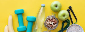 Yellow background, scattered with items - dumbells, bananas, apples, water, nuts, gym equipment